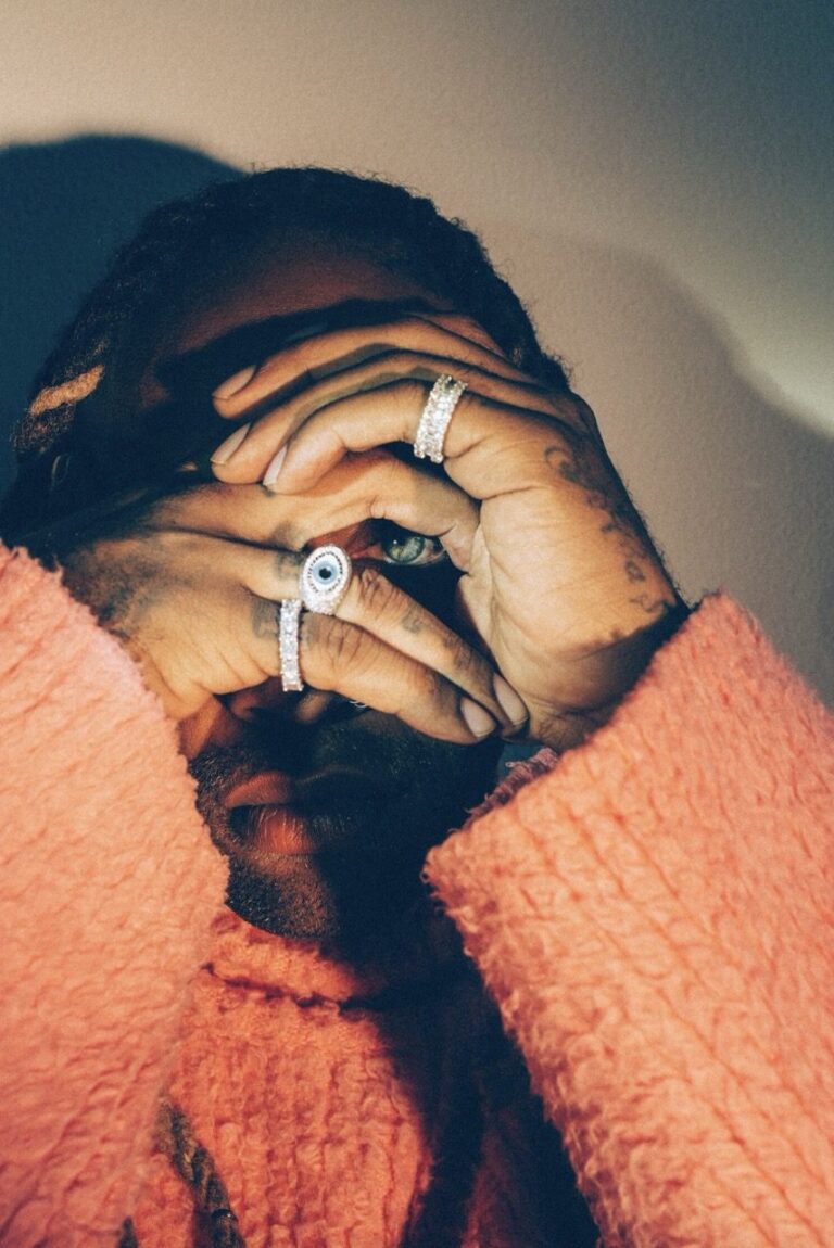 This portrait of Ty Dolla $ign (Ty $) draws a quiet but piercing line to Toni Morrison’s The Bluest Eye, a novel that interrogates desire, visibility, and the psychic violence of beauty standards shaped by whiteness. Framed by his own hands and glittering rings, Ty$’s eye peers through a self-made aperture—at once shielded and exposed.Rather than longing to be seen differently, as Morrison’s Pecola tragically does, Trotter reclaims the act of looking itself. The gesture becomes one of control and self-definition: Black vision turned inward, protected, intentional. Luxury here is not spectacle but armor; adornment does not invite consumption but marks agency. In this image, sight is not a wound but a power—refusing imposed ideals and insisting on the right to see, and be seen, on one’s own terms.